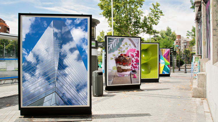 A series of electronic billboards along a street - the first image is of a skyscraper, the second of a dessert, the third of two apples, and the fourth is a colorful abstract image.