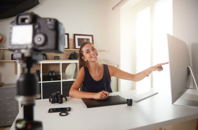 A YouTuber recording a video sitting at their desk and pointing to a monitor