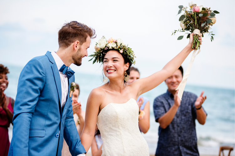 Bride and groom during wedding. The bride holds a bouquet of flowers in the air.