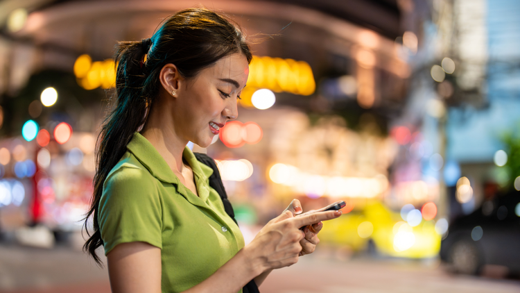 A woman stops in the street to look down at her phone. She is wearing a green blouse.