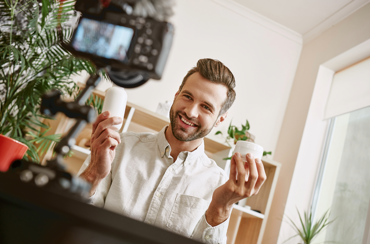 Man holding objects to camera A man holds two white plastic objects in either hand and smiles at a camera.