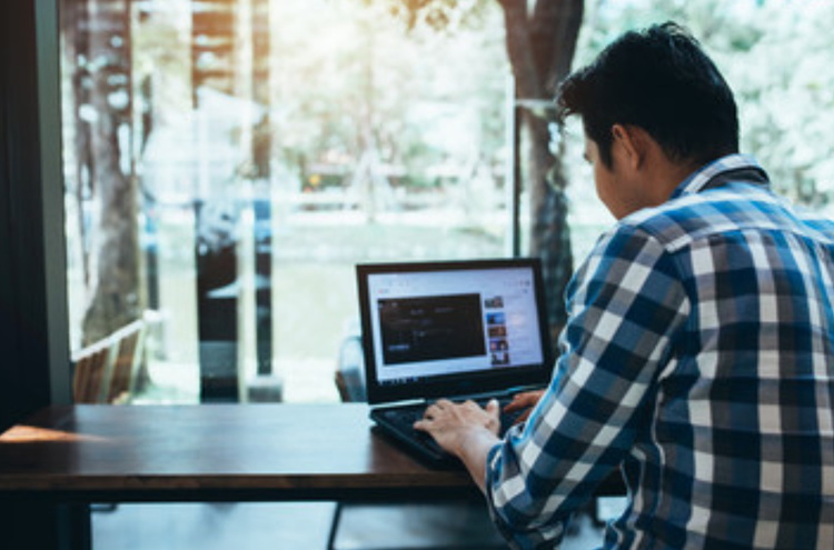 A YouTube creator with their back to the camera sitting at a table using YouTube Creator Studio on their laptop