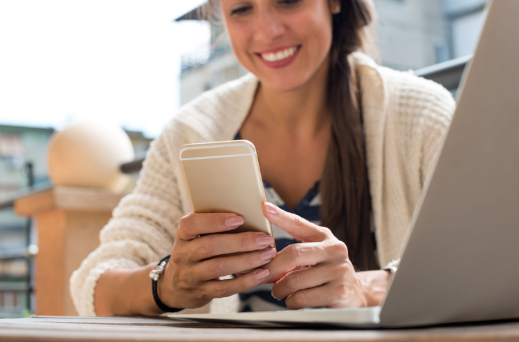 Holding phone A woman is seated, looking at the screen of a phone and smiling.