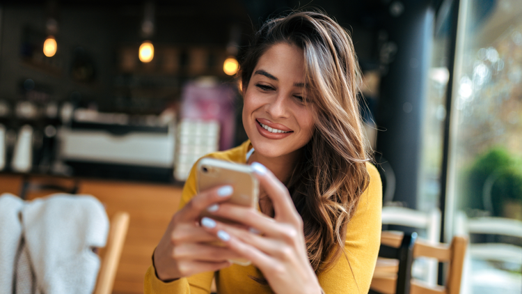 A woman wearing a yellow top smiles as she looks at her phone