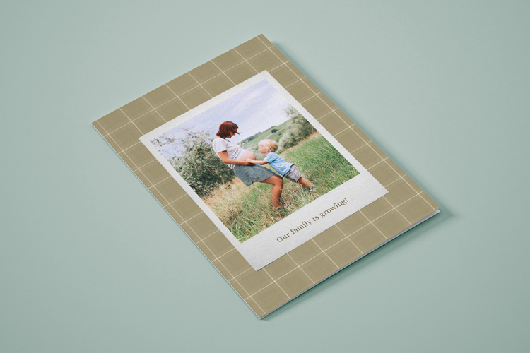 "Our family is growing!" green plaid pregnancy announcement card with an image of a child touching a pregnant person's belly in a field