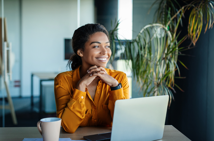 Woman smiling A woman in a yellow shirt has a laptop open in front of her on a table. She looks to her left smiling.