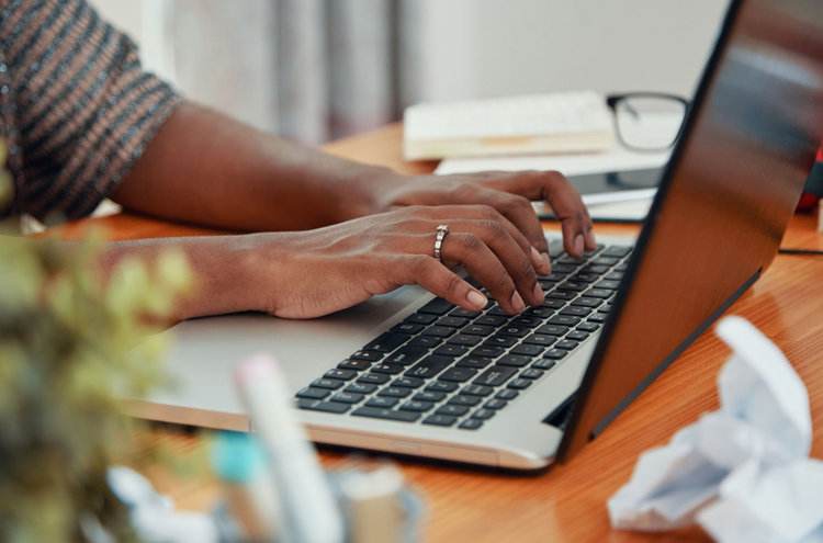 A close up of a dark-skinned person's hands responding to YouTube comments on a laptop