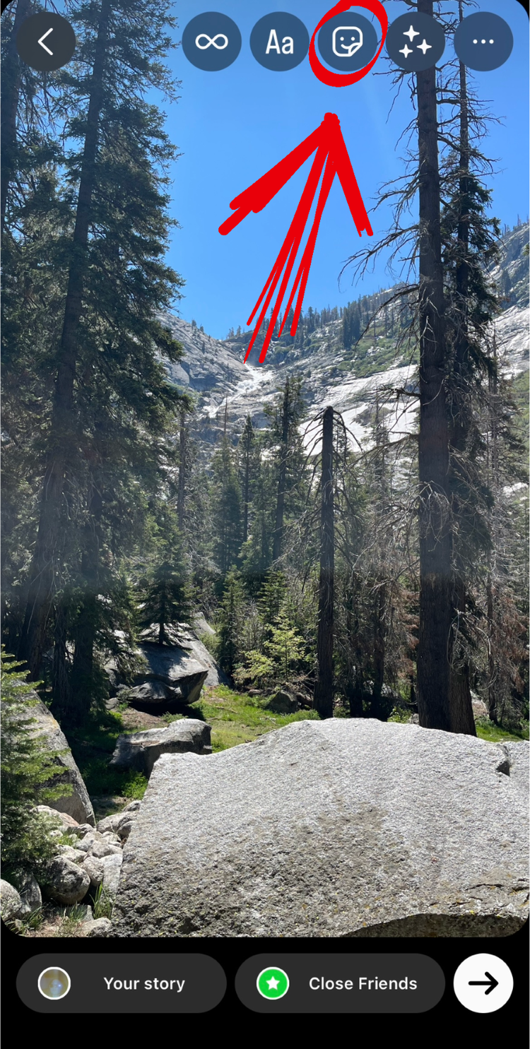 A screenshot of the Instagram Story editor with a red arrow pointing to the button where you can access stickers, GIFs, and other features