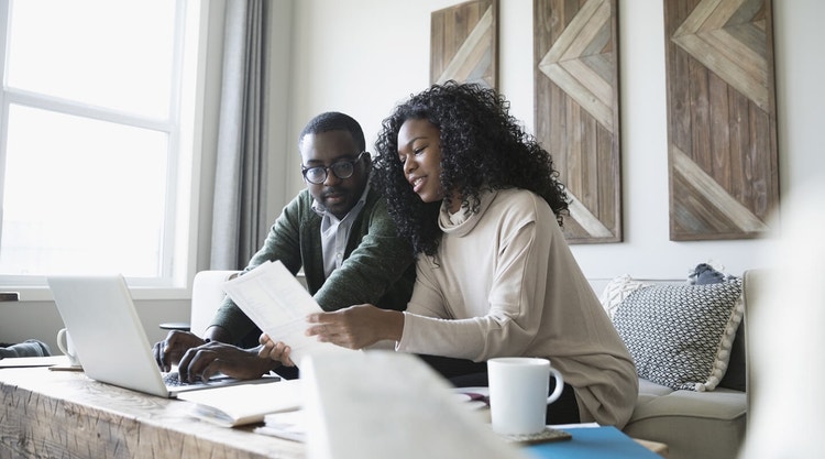 A couple sitting on a couch reviewing a paper mortgage note together