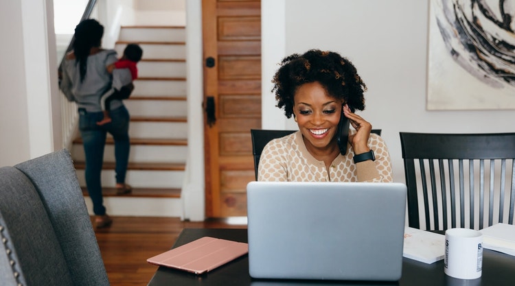 A woman talking on a mobile phone while looking at their laptop at a table