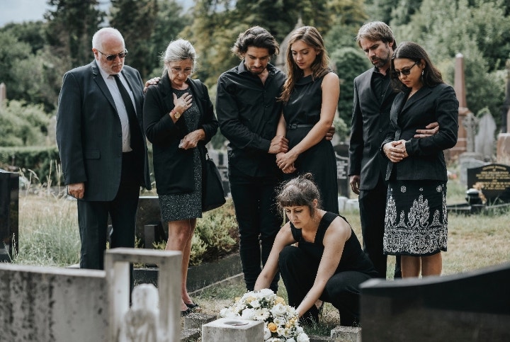 Des personnes habillées en noir se recueillent devant une tombe