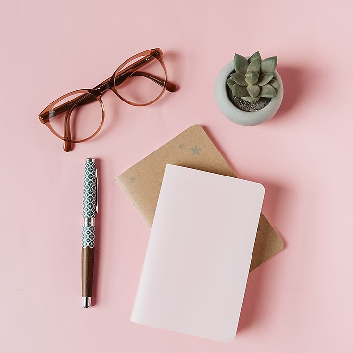 Deux carnets au formats A7 posés sur une table avec des lunettes et un stylo