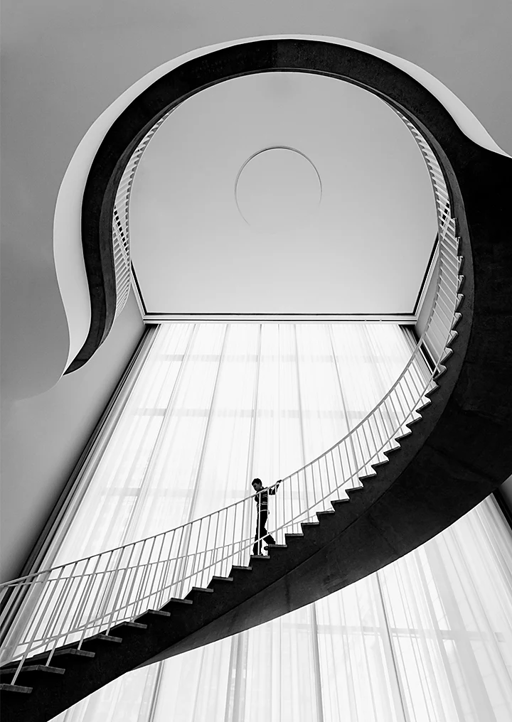 Black-and-white photo looking up at a curved modern-looking staircase