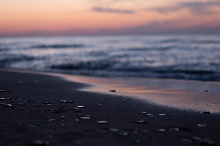 An anamorphic beachside view at sunset with the rocks in the foreground in focus and the sunset and sea out of focus