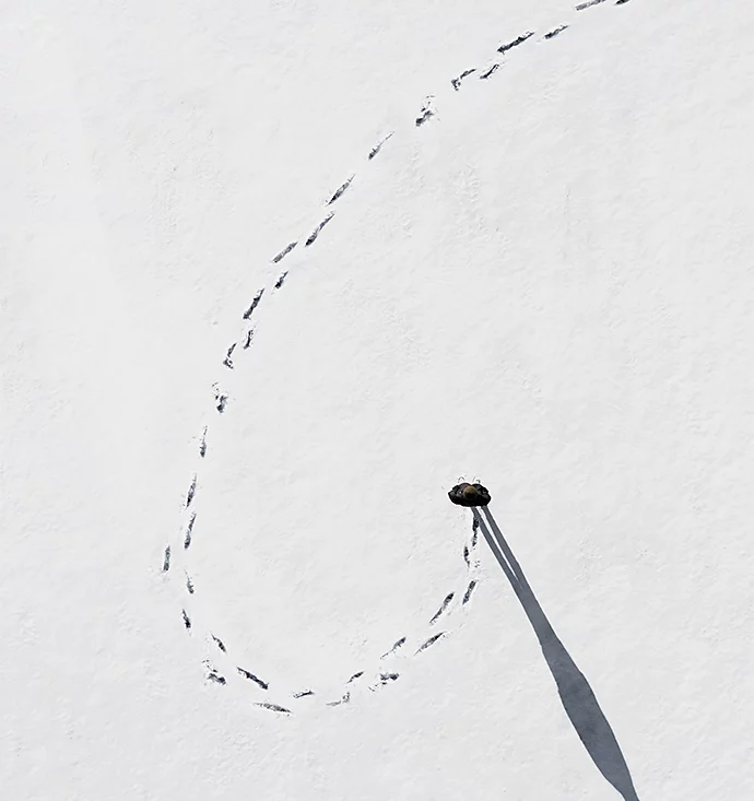 An overhead photo of a person walking in a curved line and then making a U-turn in the snow with a trail of footprints behind them