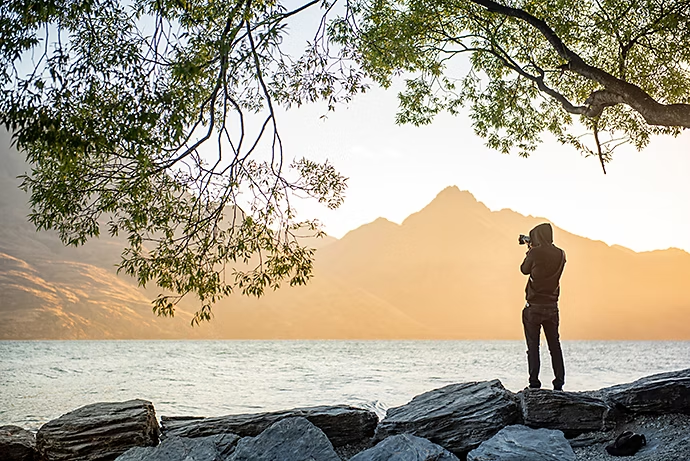 young-male-photographer-looking-at-scenery-of-lake-wakatipu-during-golden-hour-sunset-in-queenstown-south-island-new-zealand-travel-and-landscape-photography-concepts