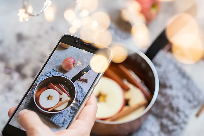 Personne photographiant des bâtons de cannelle et des rondelles de pomme dans une casserole