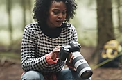 A person kneeling in a forest while looking at their camera