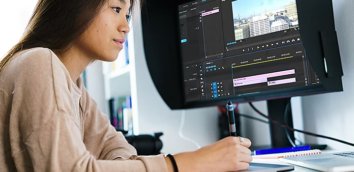 Personne assise à un bureau réalisant le montage d’une vidéo sur un ordinateur portable connecté à un second écran