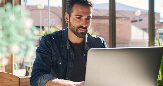 A person sitting at a sunlit table and working on their laptop