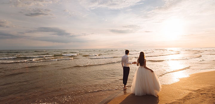 Dreamy wedding photo of a bride and groom walking on the beach into the horizon.