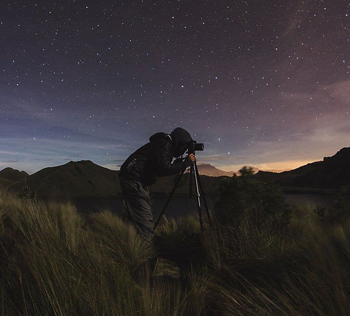 A photographer taking a photo with a camera on a tripod at nighttime in the middle of a field