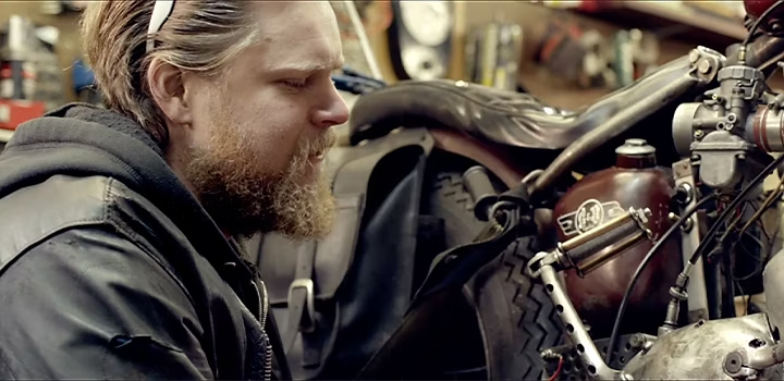 A person crouched in front of a motorcycle for a documentary film