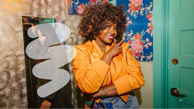 A woman in an orange jacket and jeans standing in front of a mirror, checking her appearance.