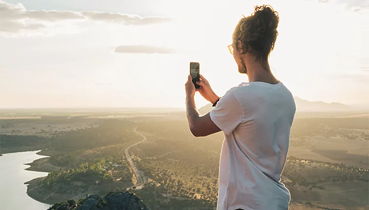 A person taking a photo of the view from a mountain hillside