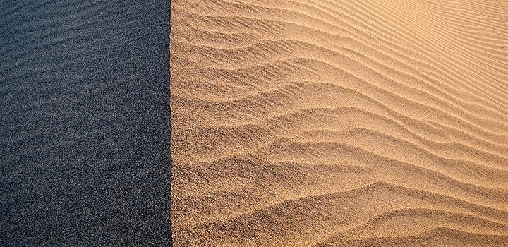 A sand dune within the sunlight with part of it in the shadow