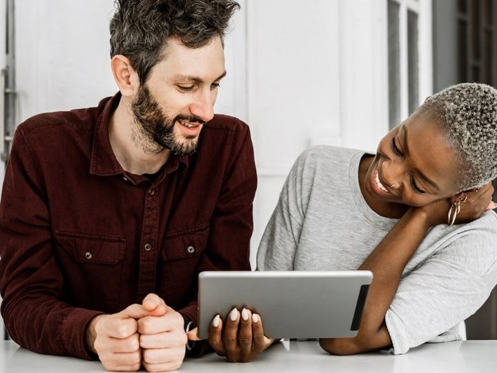 An image of two people standing at a table and looking at a tablet.