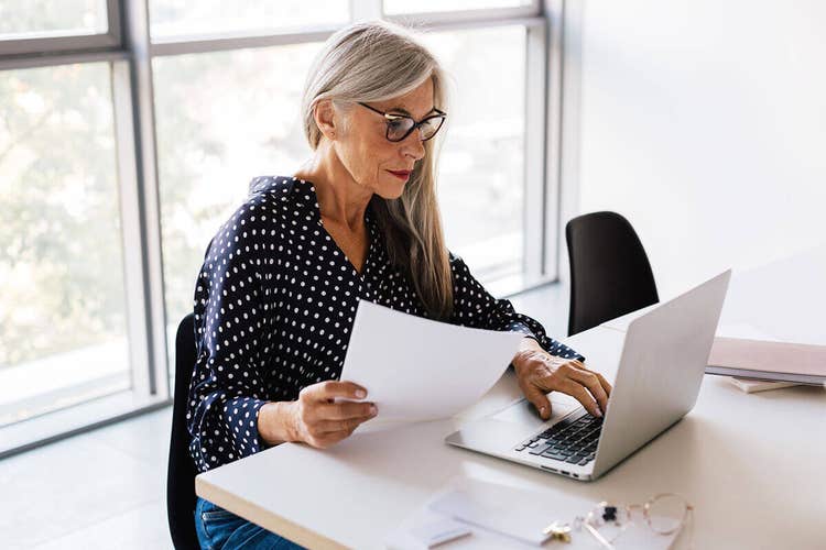 A landlord sitting at a desk reviewing a printed apartment lease agreement while using their laptop