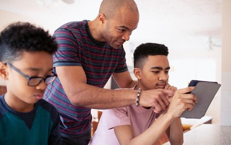 A parent looking over the shoulder of their child at an e-doc before signing with Acrobat Sign as their other child sits next to them