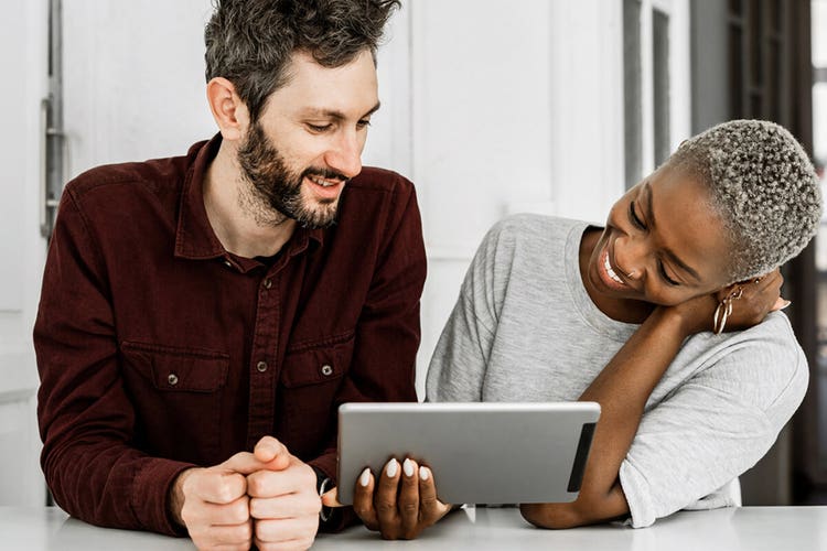 An image of two people standing at a table and looking at a tablet.