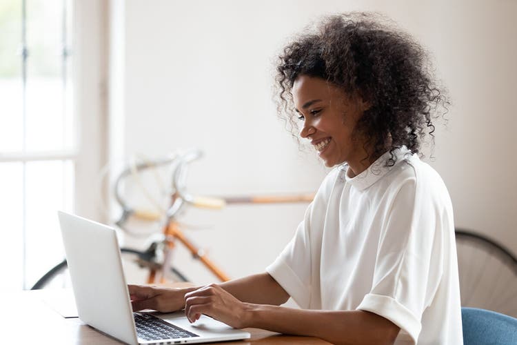 A woman in a white shirt at a desk using a laptop to sign an NDA with Adobe Sign.