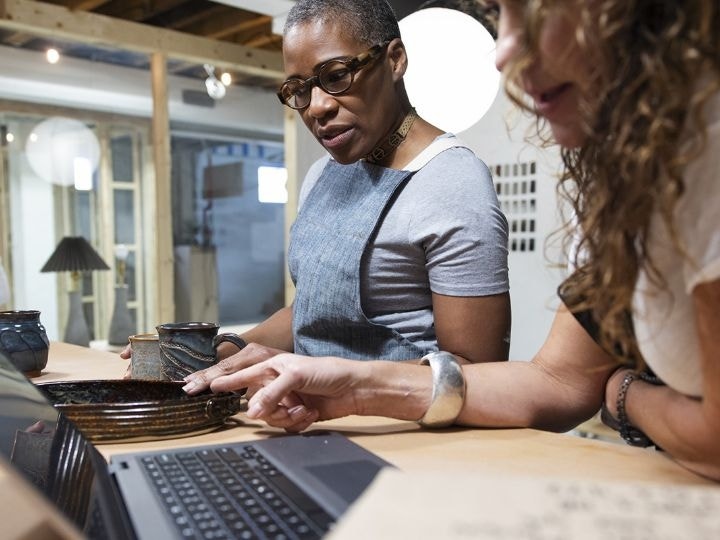 An image of a person standing at a desk and looking down at a laptop.