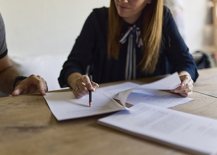 A person holding a pen while going over documents with a colleague