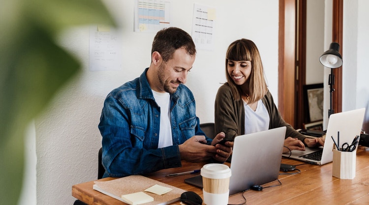 Two people sitting next to each other at a table with their laptops