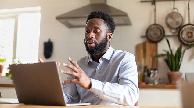 A person working remotely from their kitchen by participating in a video conference call on their laptop