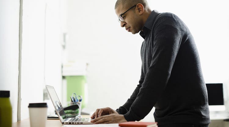 A person standing at a desk using their laptop