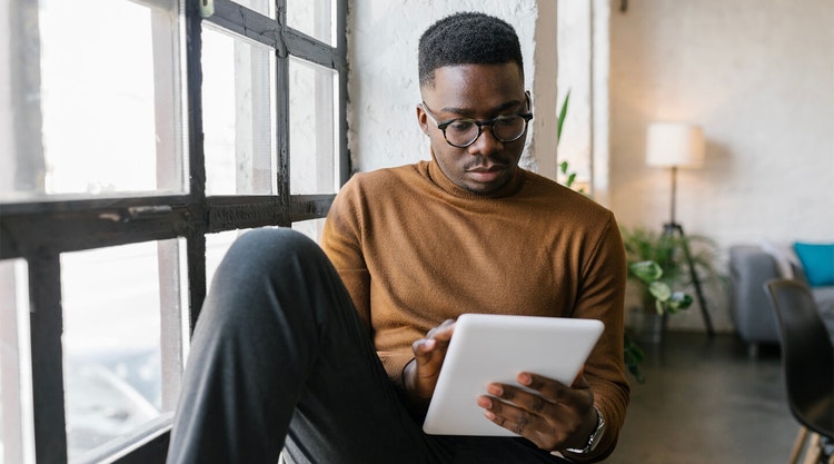 A person sitting beside a window looking over an e-doc on their tablet using Acrobat Sign