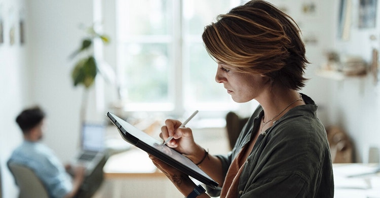 A person writing on a tablet with a stylus while standing in their home office