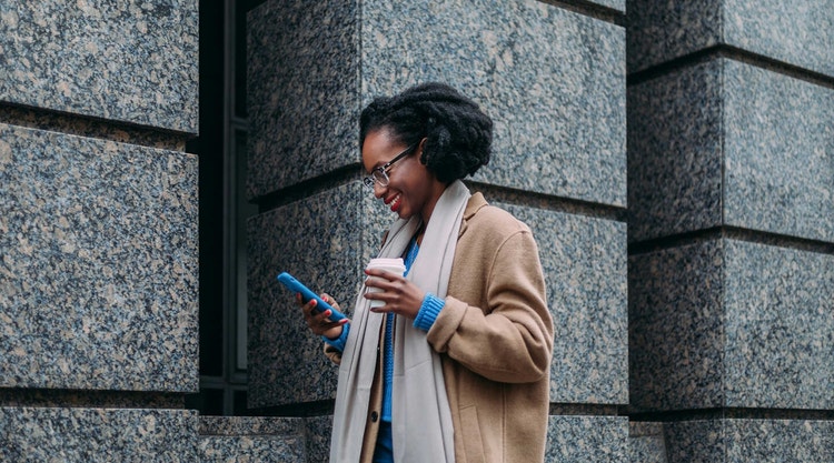 A woman filling out a signature using their mobile phone while holding coffee outside a building