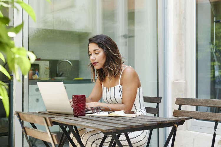 Woman sitting outside in a white jumpsuit while reviewing a landscape contract on her laptop