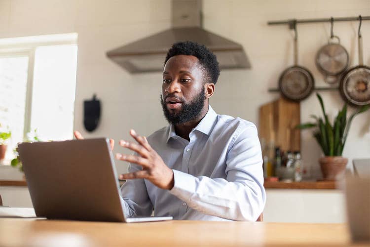 A person working remotely from their kitchen by participating in a video conference call on their laptop