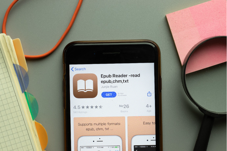 A phone on an office desk displays an app search for an ePub reader, indicating the user's intent to download it.