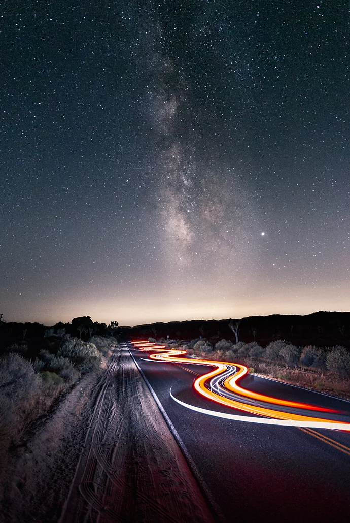 Light trails hovering over a desert roadway from a car driving through