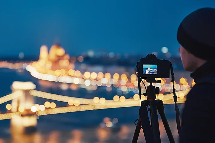 A photographer taking a photo of city at night with their camera on a tripod