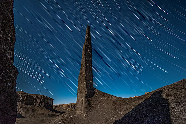 Star trails behind a tall rock formation