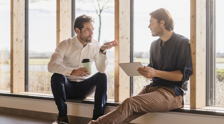 Two men sitting on a window sill discussing confidential information.